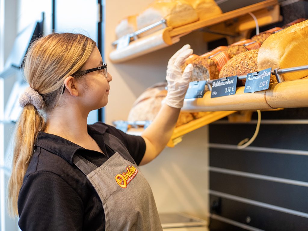 Verkäuferinnen nimmt Brot aus der Auslage | Dördelmann Backwaren Vertriebs GmbH & Co. KG – An der Bewer 10 – 59069 Hamm