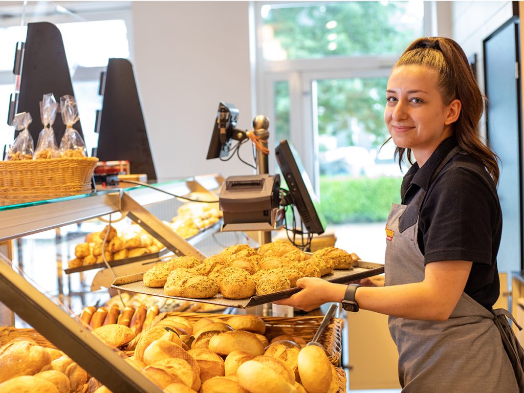 Verkäuferin legt Brötchen in die Auslage | Dördelmann Backwaren Vertriebs GmbH & Co. KG – An der Bewer 10 – 59069 Hamm
